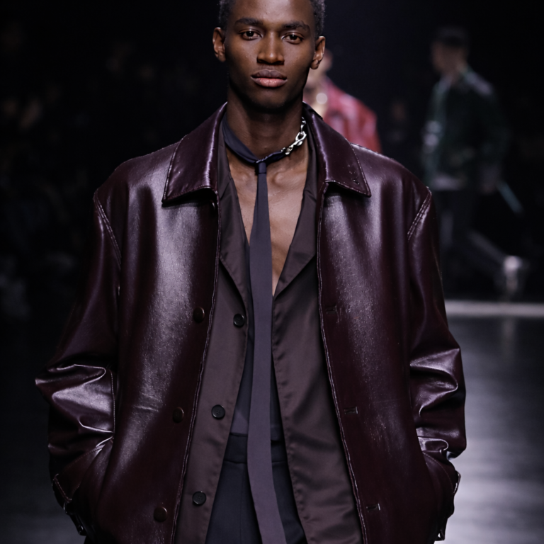 AI generated Male runway model wearing a burgundy leather coat and sheer shirt during a luxury fashion show runway presentation