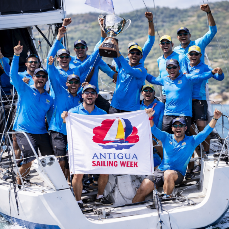 AI-generated image of a jubilant sailing crew celebrating victory during Antigua Sailing Week aboard a racing yacht, raising a trophy and event banner in a 4:3 editorial sports scene.