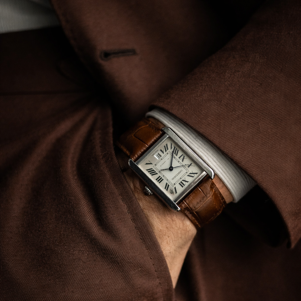 AI-generated image of a Cartier Tank watch with Roman numeral dial and leather strap, worn under a tailored suit sleeve.