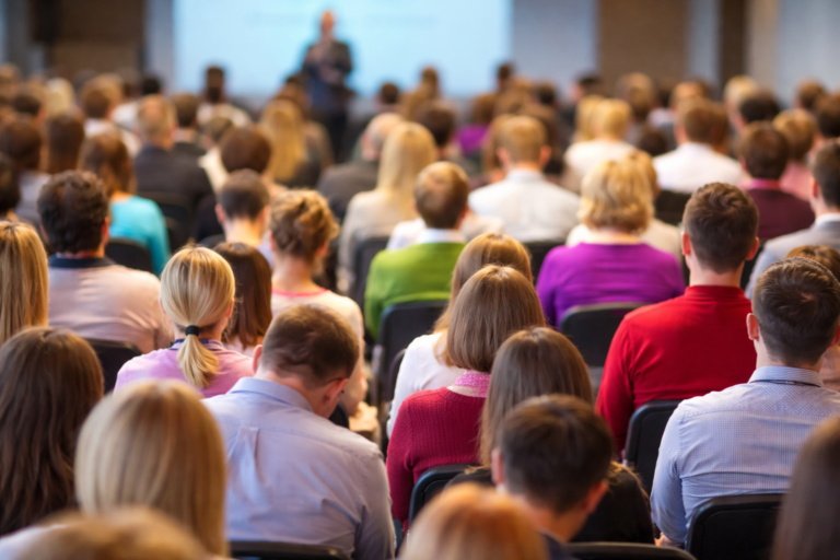 AI-generated image of a large audience attending a business and finance conference keynote presentation in a modern event hall.
