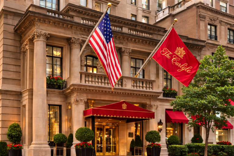 AI generated luxury hotel entrance in Manhattan with American flag and classic architectural façade Caption: Historic Manhattan hotels continue to define timeless urban luxury hospitality.
