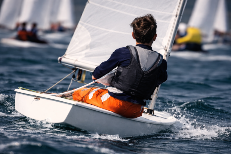 AI-generated image of a young sailor racing a small dinghy during a competitive sailing regatta, with multiple sailboats visible in the background.